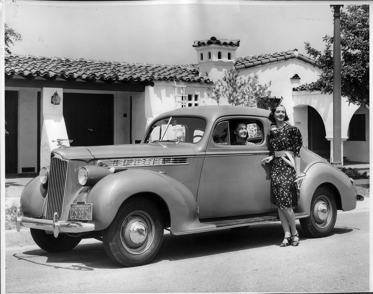 Women posing with 1940 Packard business coupe, parked on street in front of house
