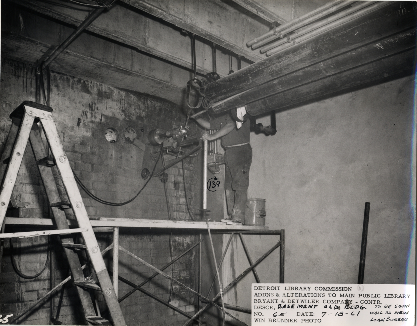 Construction worker installing pipes in basement, Main Library