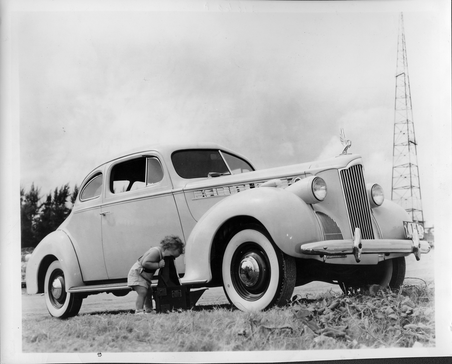 1940 Packard club coupe parked on grass, toddler beside car