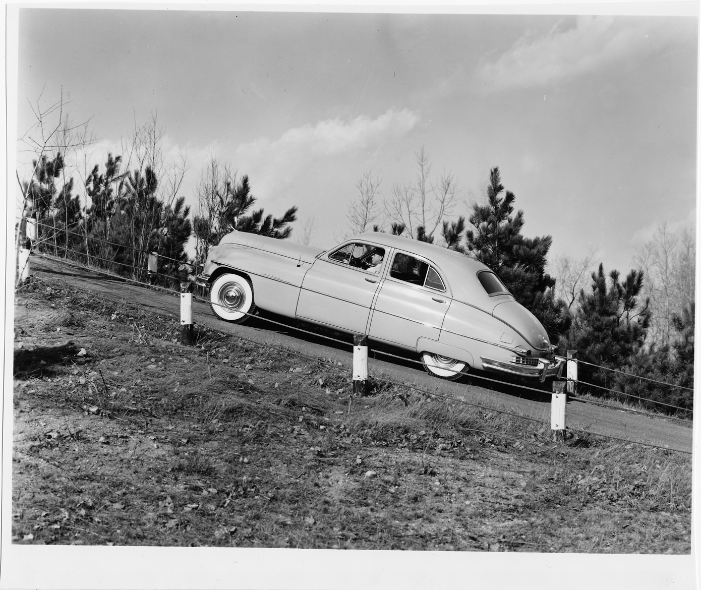 1949 Packard sedan, left side view, driving up steep hill, man behind wheel