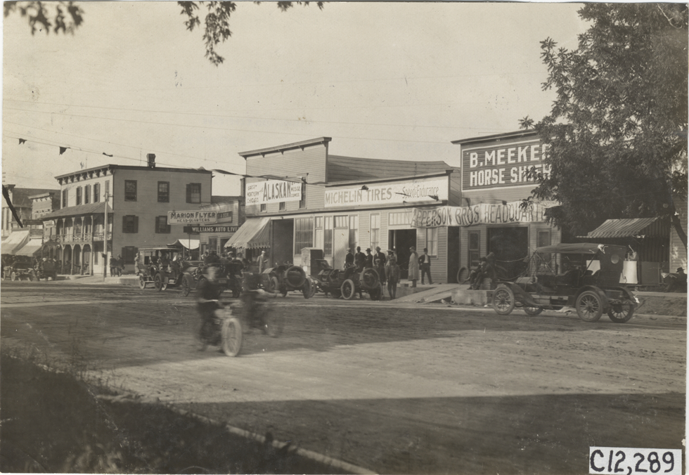 Racecars and automobiles parked in front of commercial buildings, 1909 Crown Point races