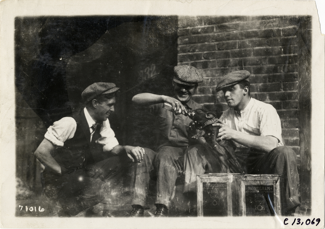 Three men feeding piglet, 1911 Fairmount Park races