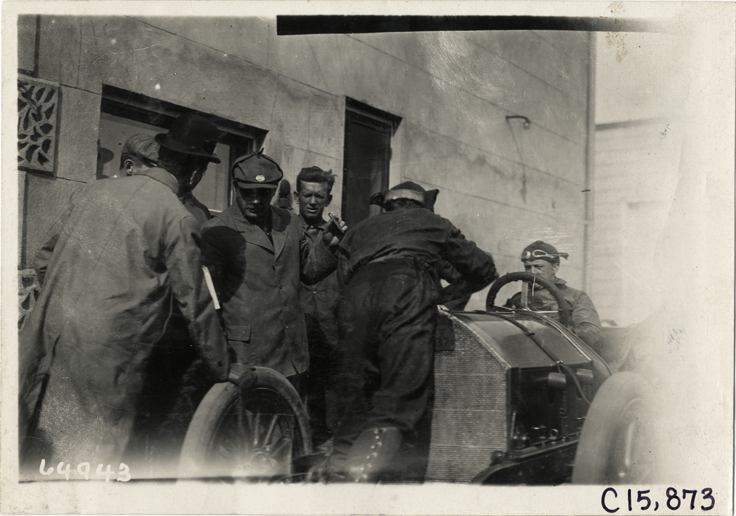 Officials conferring in front of racecar, 1910 Vanderbilt Cup races