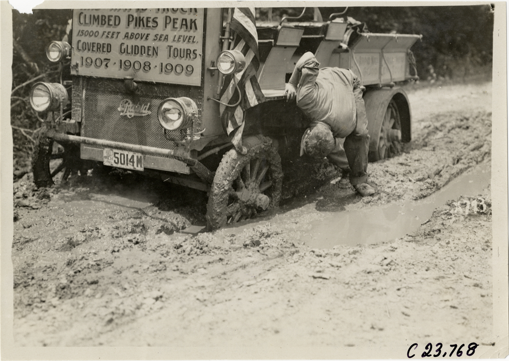 Driver examining tire of Rapid truck stuck on muddy road, 1910 Glidden Tour