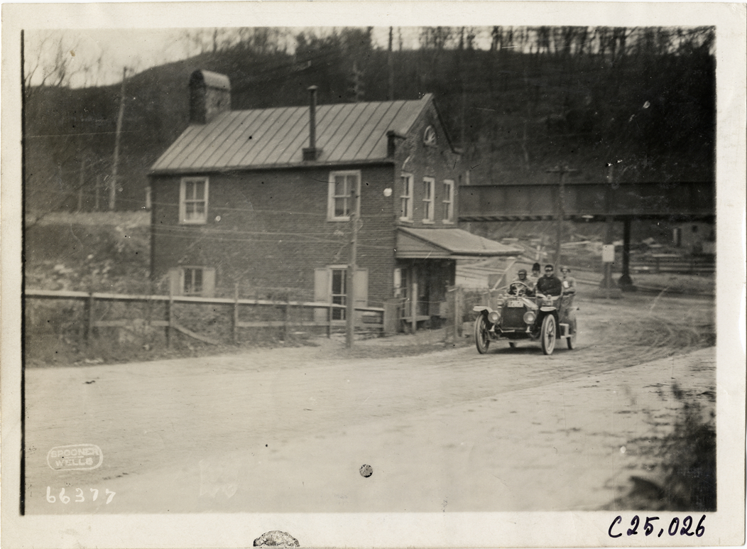 Motorists in automobile passing brick building, 1910 Harrisburg Endurance Run