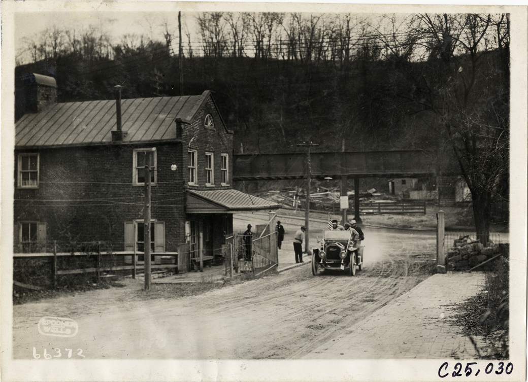 Motorists in automobile passing brick building, 1910 Harrisburg Endurance Run