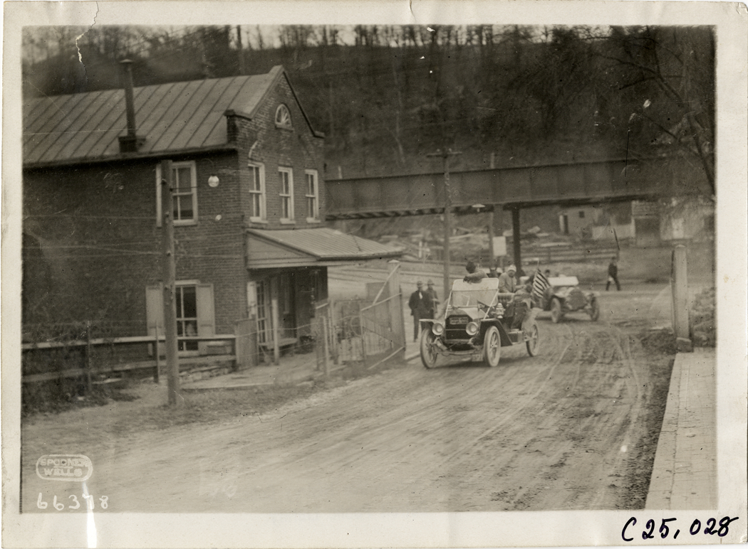 Motorists in automobile passing brick building, 1910 Harrisburg Endurance Run