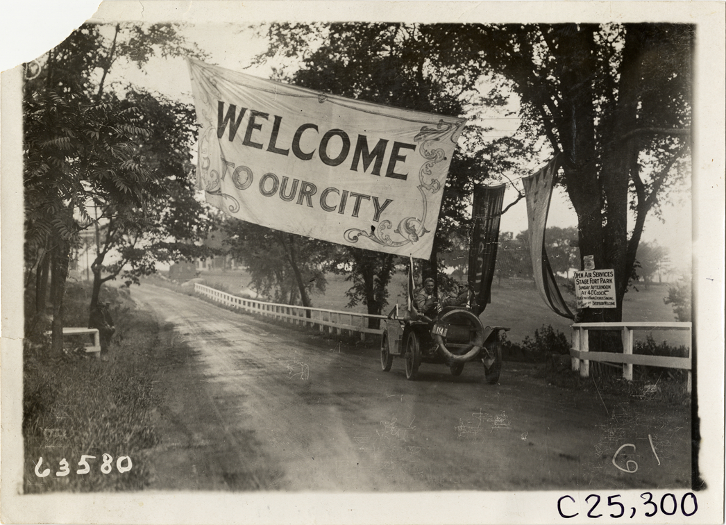 Motorists in automobile approaching banner over road at Gloucester, Massachusetts, 1910 Munsey Historic Tour