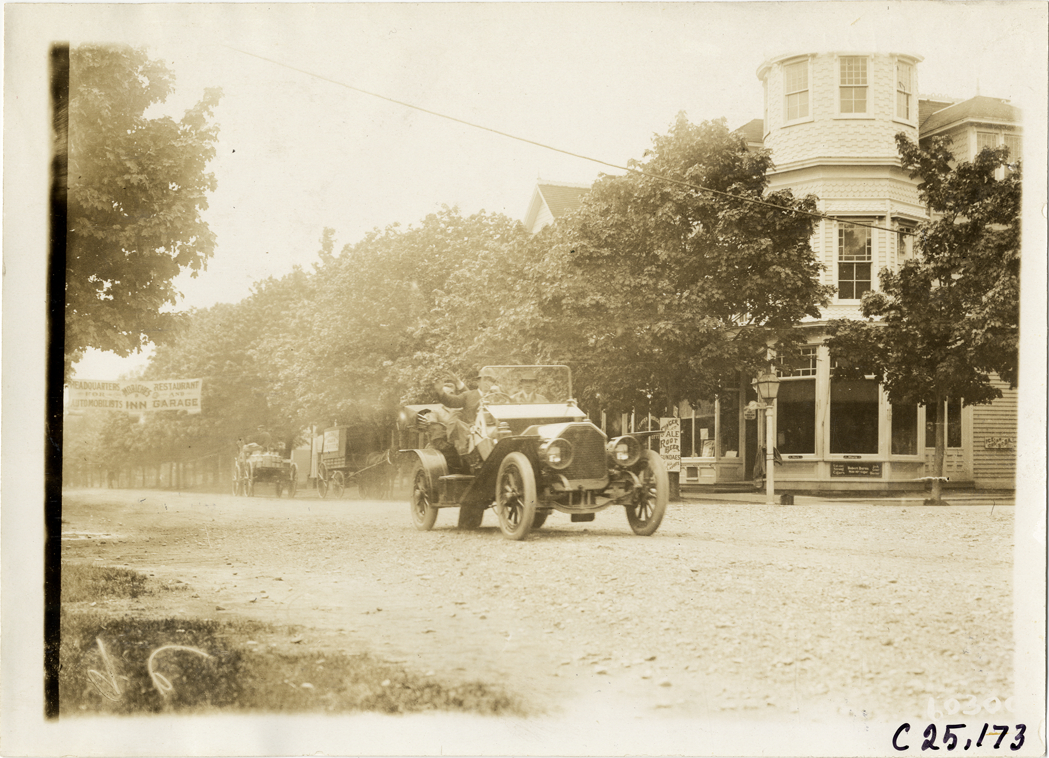Motorists in automobile traveling past stores, 1910 Long Island Endurance Run
