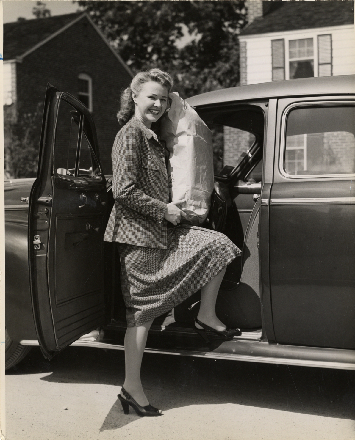 Woman holding bag of groceries and posing next to automobile