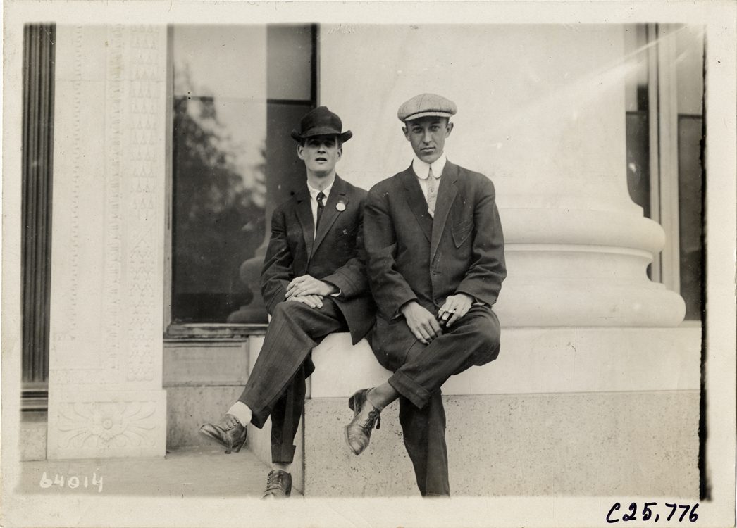 Two men posing in front of column, 1910 Munsey Historic Tour