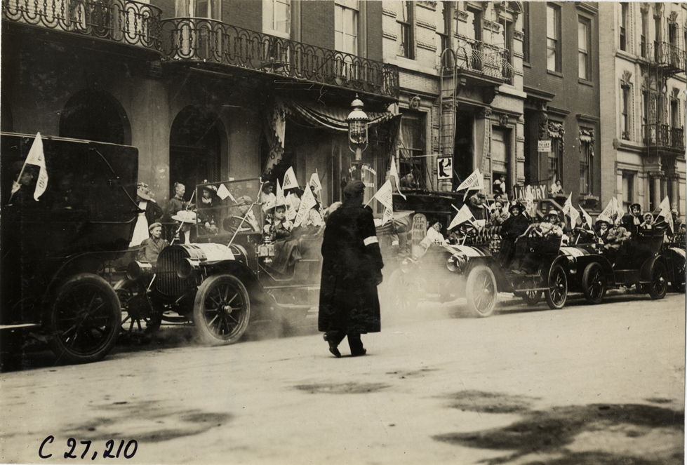 Official walking past automobiles lined up in street, 1909 New York Orphans Day outing